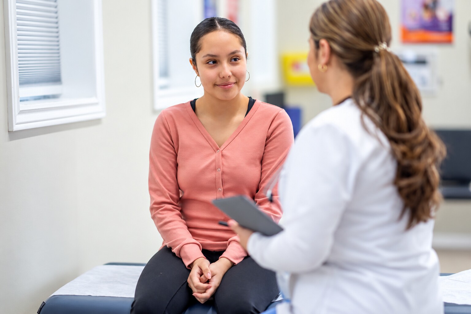 A teenage girl smiling as she talks with her doctor in an exam room